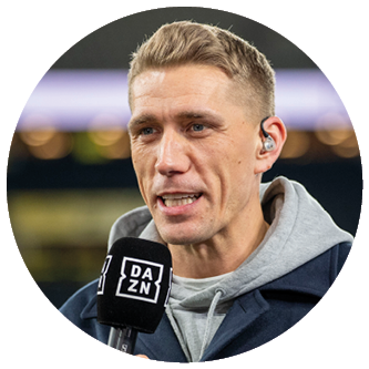 Eine Person mit kurzem Haar tr gt einen Kapuzenpullover unter einem Mantel und spricht in ein Mikrofon mit dem DAZN-Logo, w hrend sie ein In-Ear-Monitor tr gt. Beschreibung von KI generiert