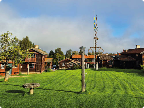Mehrere traditionelle Holzh user stehen auf einer gro en gr nen Wiese unter einem bew lkten Himmel. Beschreibung von KI generiert