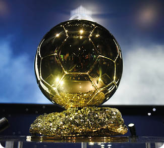 Der goldene Ballon d'Or steht auf einem funkelnden Sockel vor einem verschwommenen Hintergrund mit blau-wei en Farbt nen. Beschreibung von KI generiert